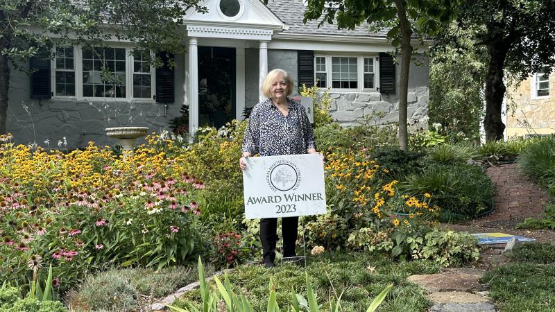 woman standing in yard with award winner 2023 sign