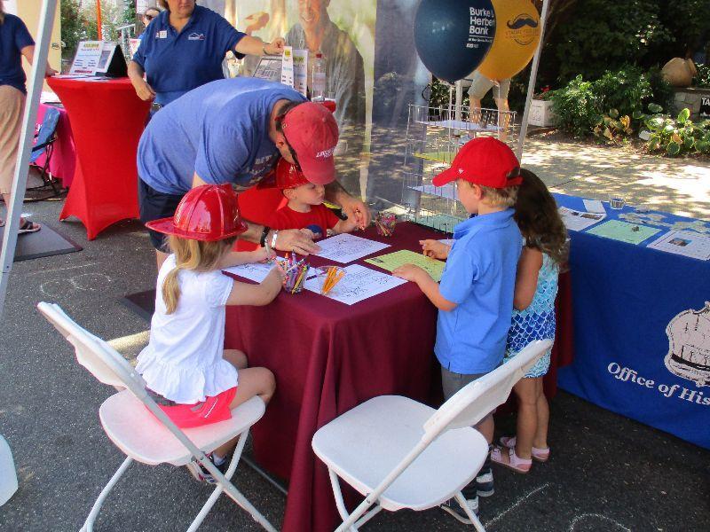 Four children with an adult seated at an outdoor table coloring.