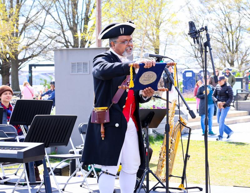 The town crier, in full costume complete with tricorn hat, standing on a stage with a microphone and reading the 275th anniversary proclamation 