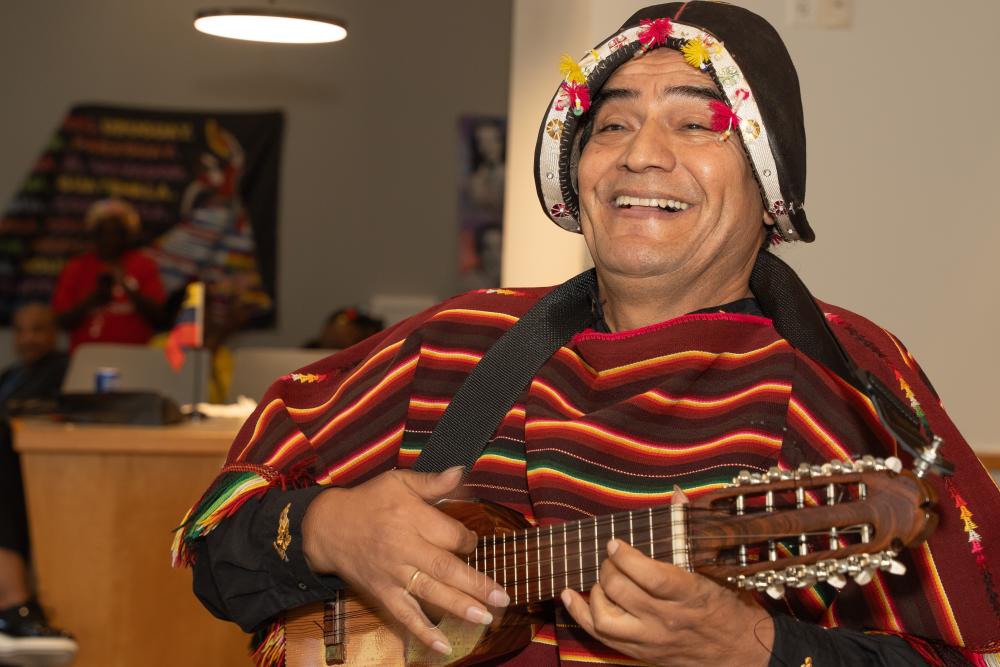 Man with guitar and decorated hat with striped shirt smiling