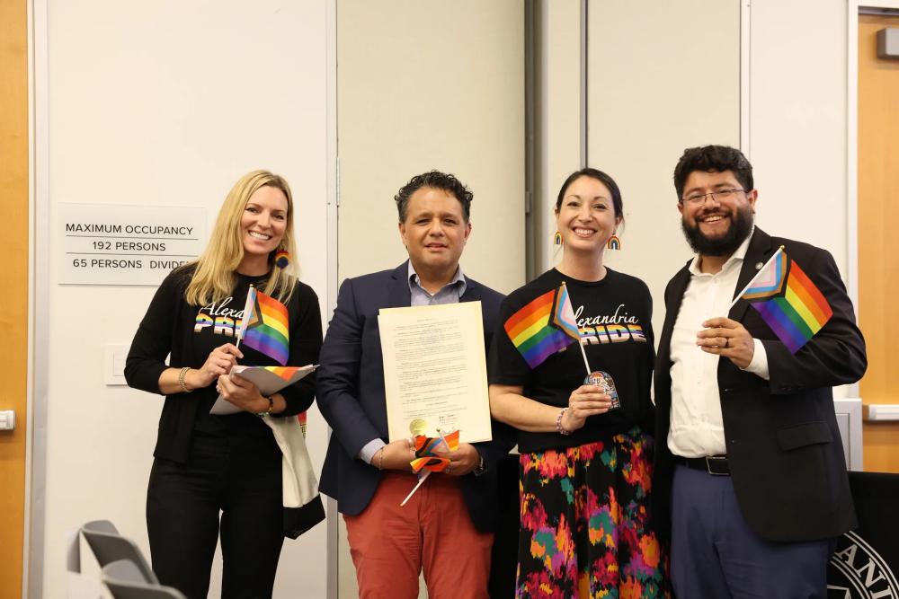 Four people posing with proclamation and pride flags
