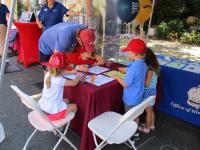 Four children with an adult seated at an outdoor table coloring.