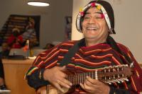 Man with guitar and decorated hat with striped shirt smiling