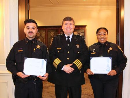 Sheriff in formal uniform standing between two deputies, both wearing dark blue uniforms and holding award certificates