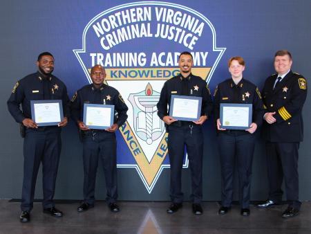 Sheriff in formal blue uniform and dour deputies wearing blue uniforms, holding graduation certificates and smiling