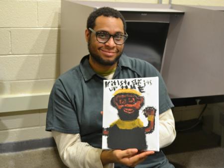 Man wearing a green jumpsuit, smiling, and holding a painting he created of his grandfather