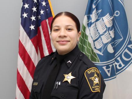 Official portrait of Deputy Hernandez wearing blue uniform with U.S. and Alexandria flags in background