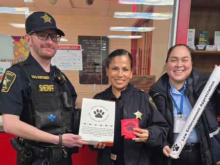 Two deputies and a firefighter smiling and holding small gifts at a school
