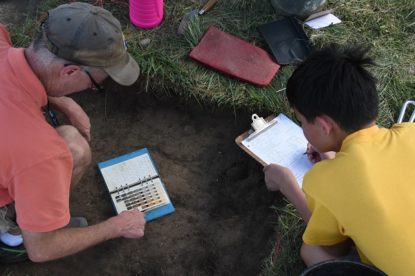 An archaeologist and summer camper record soil color, using a Munsell Color Chart