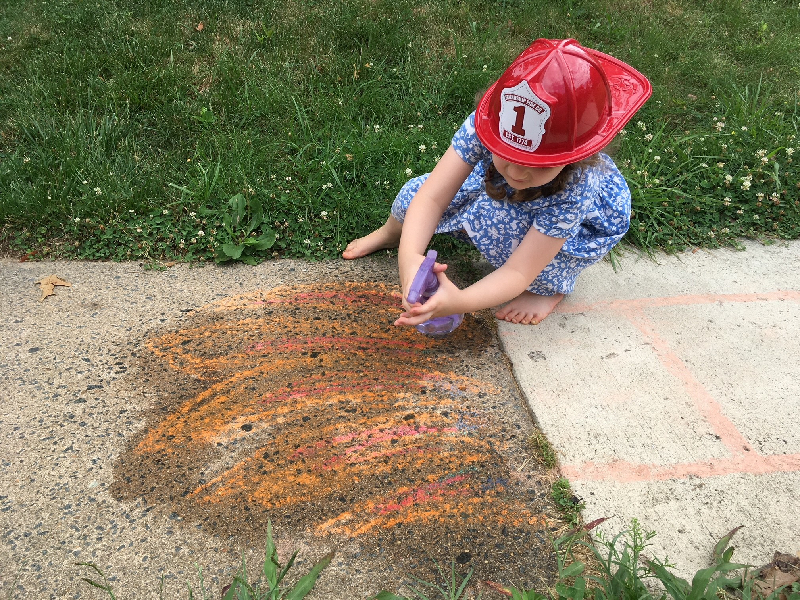 A child sprays water on chalk flames drawn on a sidewalk.