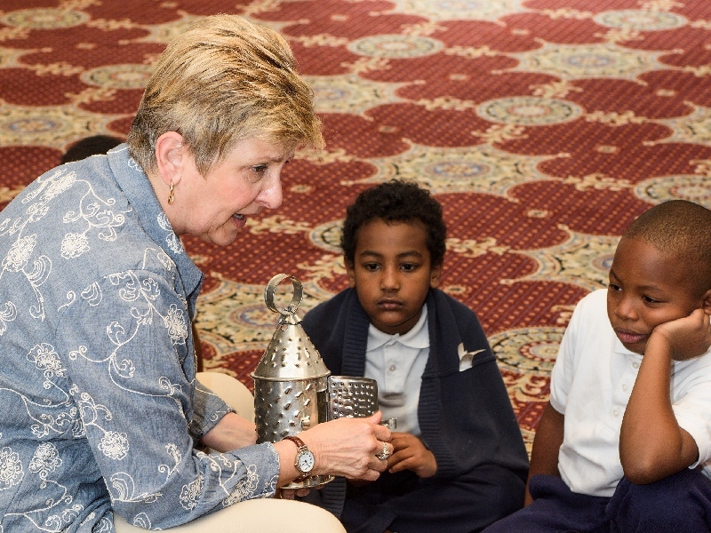 A volunteer shows students a tin lantern during a program.