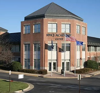 A red brick building with NVCJ ACADEMY on the front, partially blocked by a flagpole waving the American flag