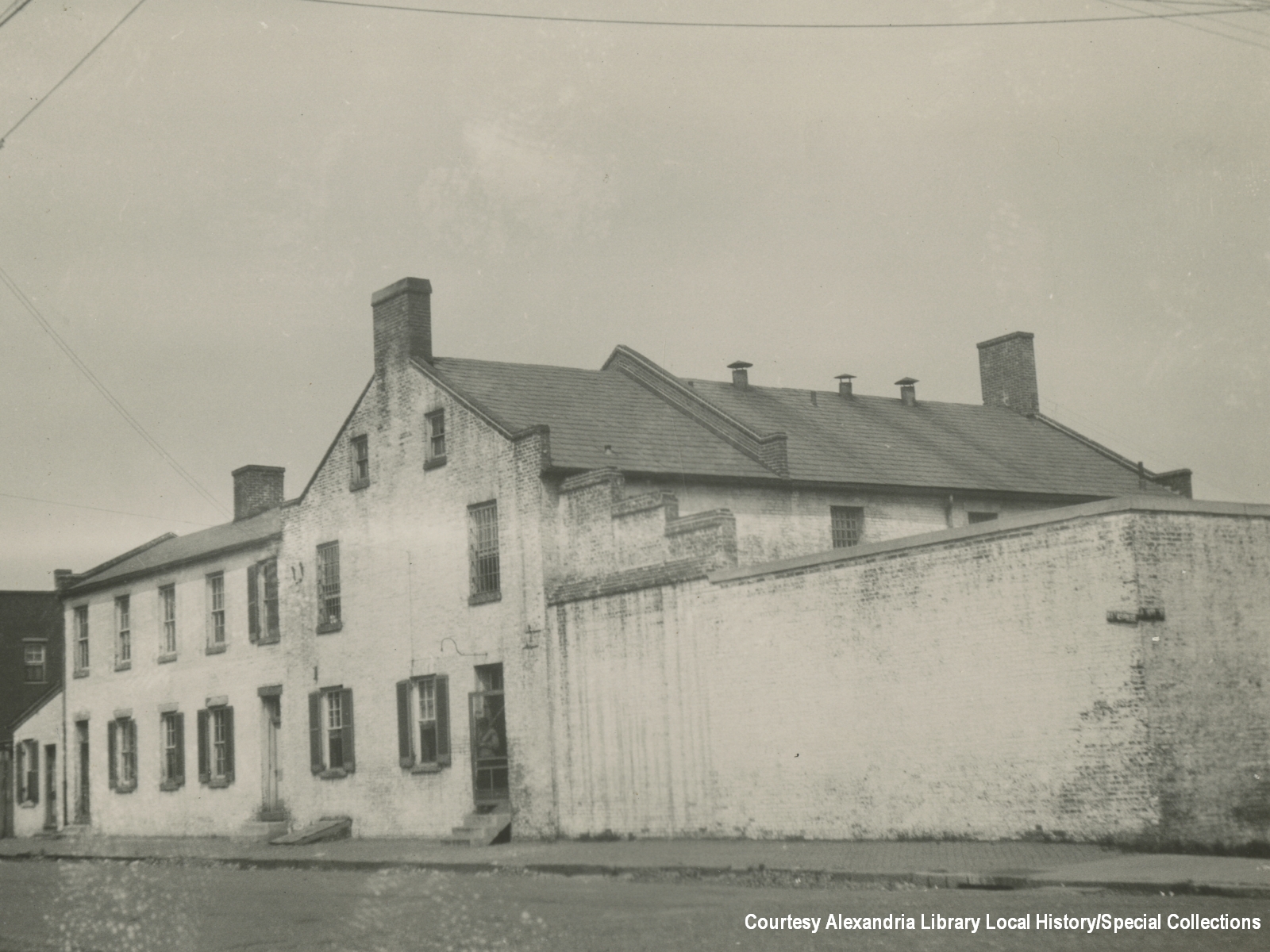 Historic black and white image of old city jail with brick wall, all painted white