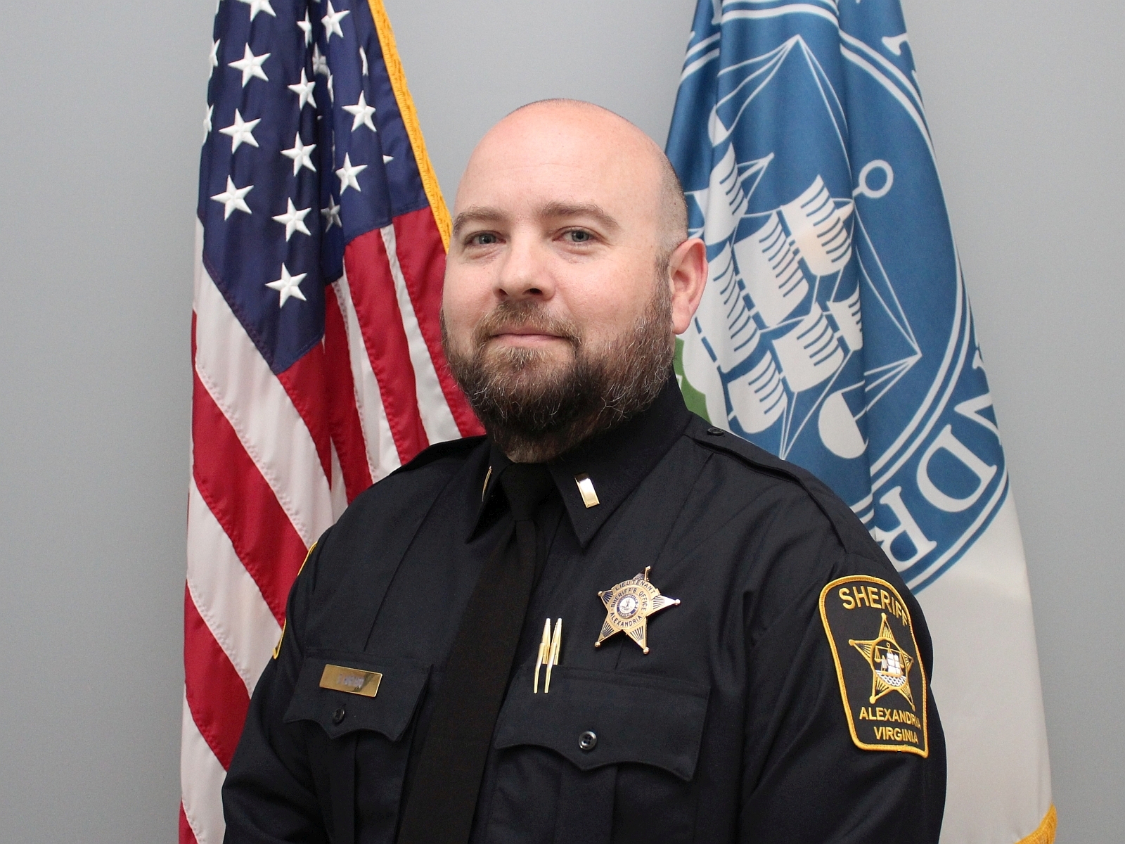 Official portrait of Lieutenant Hagar wearing blue uniform with U.S. and Alexandria flags in background
