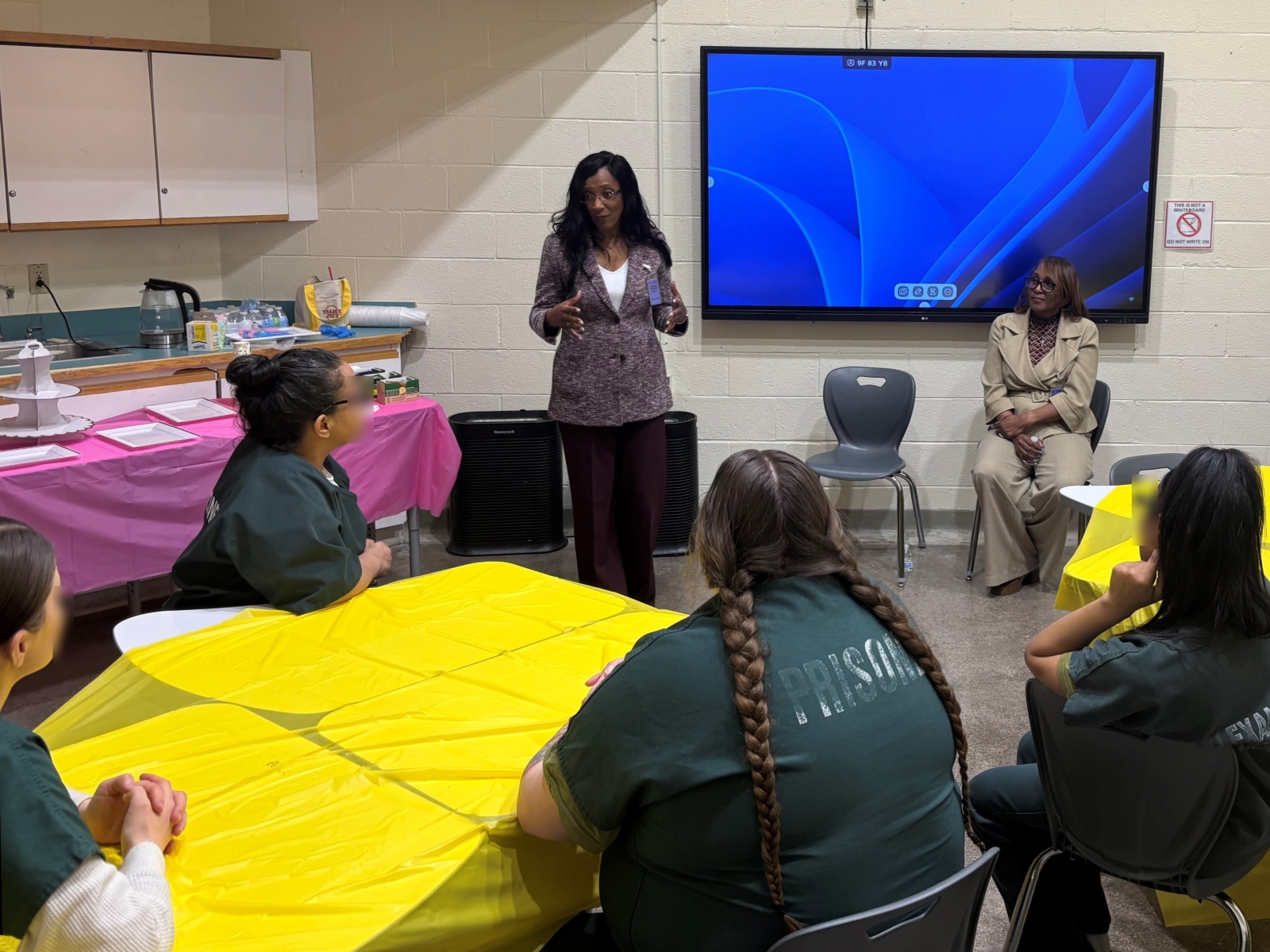 Two judges in civilian attire speaking with inmates who are wearing green uniforms and are seated at tables