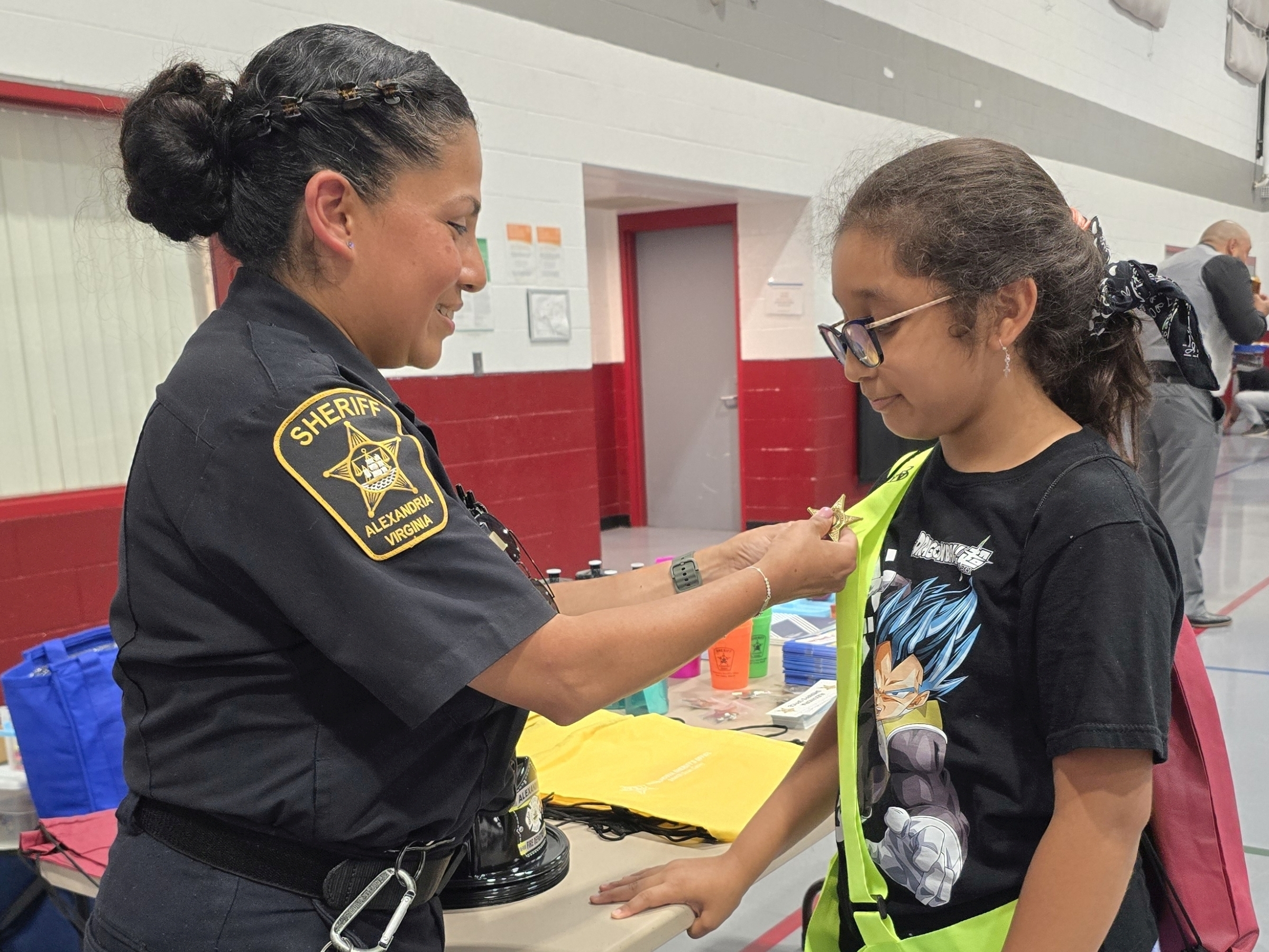 Sheriff's sergeant in blue uniform pinning a badge on the safety patrol belt of an elementary school student at a community event