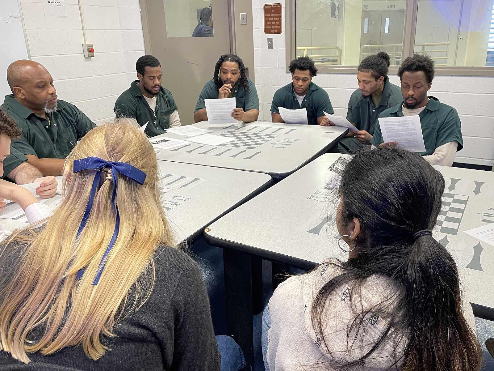 six inmates wearing green jumpsuit and two college students reading and discussing a short story
