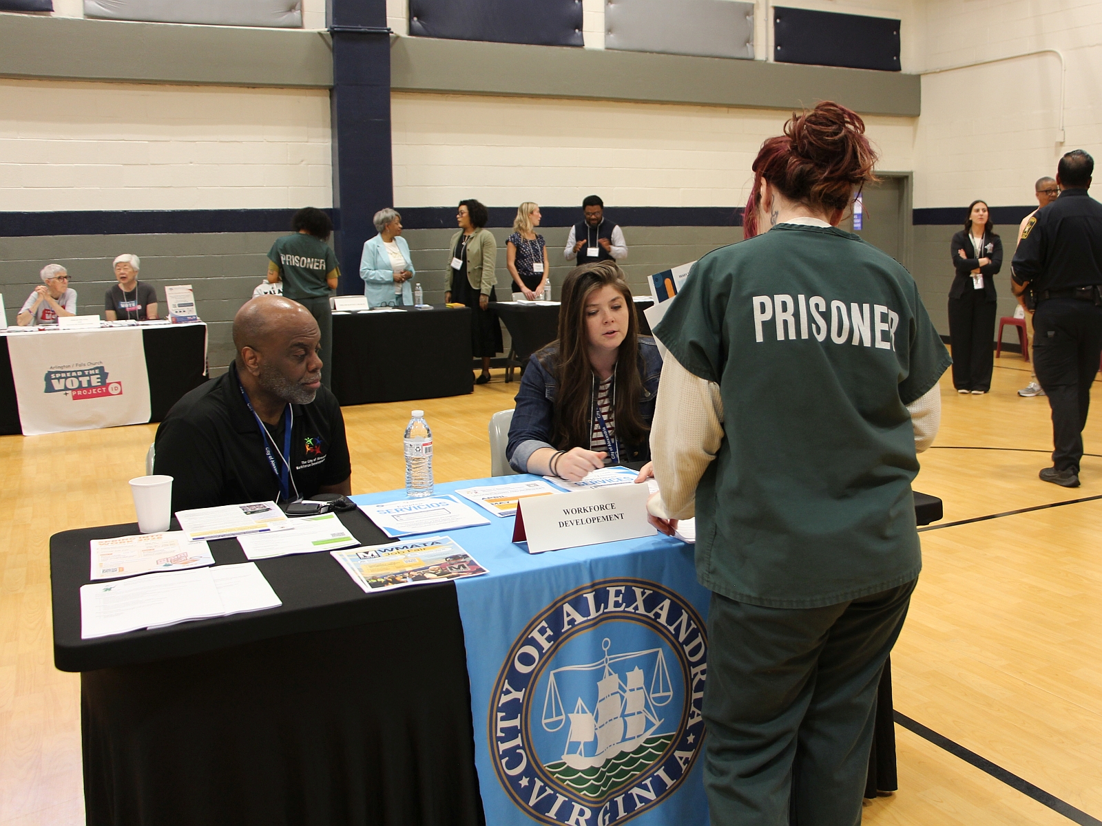Inmate in green uniform that says Prisoner on the back speaking with two members of the Workforce Development team at the Reentry Resource Fair