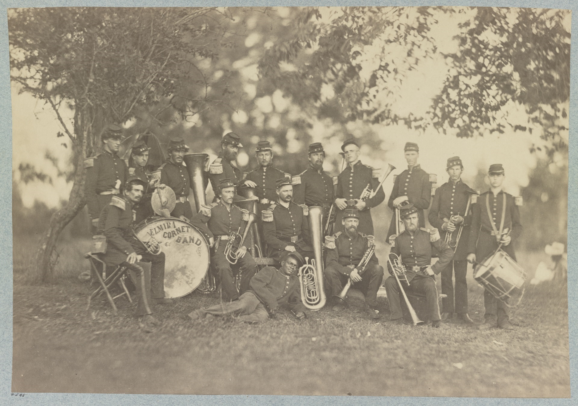 Fifteen musicians pose with their instruments in this black-and-white photograph. The drum is labeled “Emira Cornet Band.”
