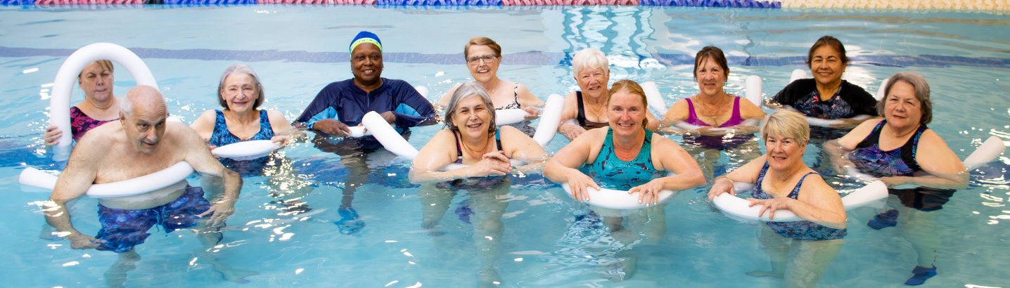 Group of seniors in the pool with pool noodles smiling at the camera