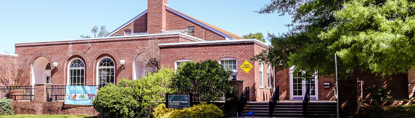 Front view of the Oswald Durant building, showcasing brick and trees on the right side and bushes in the front