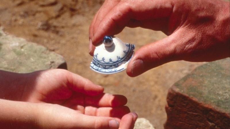 Adult handing toy teapot lid to a child. Image used on poster for Virginia Archaeology Month