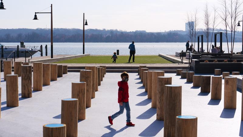 Child walking between the wooden pillars of varying heights in Groundswell. The Potomac River is in the background.