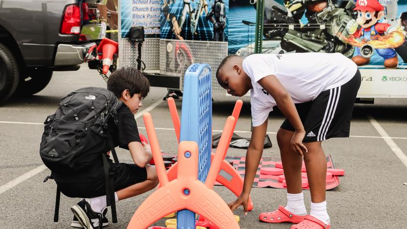A boy in black with a black backpack and a boy in white are playing lawn-size Connect 4