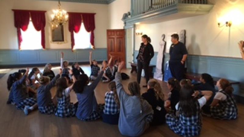 Image of students with hands raised gathered around two tour guides in historic ballroom of Gadsby's Tavern Museum. 