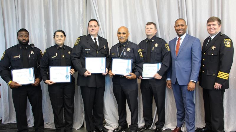 five uniformed law enforcement holding award certificates standing next to Aaron Gilchrist and Sheriff Sean Casey