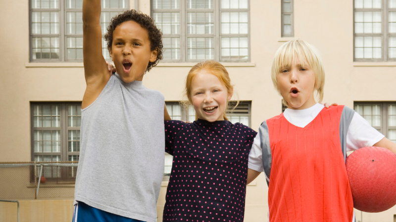 three kids looking excited with child on right holding a dodgeball