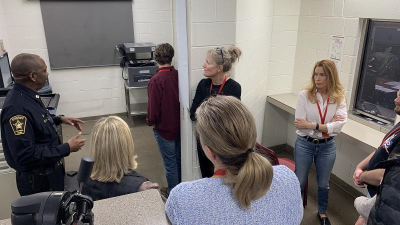 Uniformed Sheriff's Office commander speaking to six civilians inside the booking area of the jail