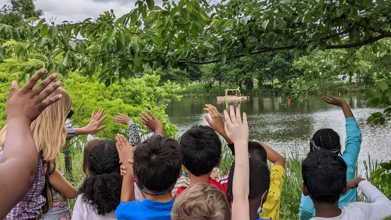 a group of Alexandria children raise their hands to participate in a nature activity