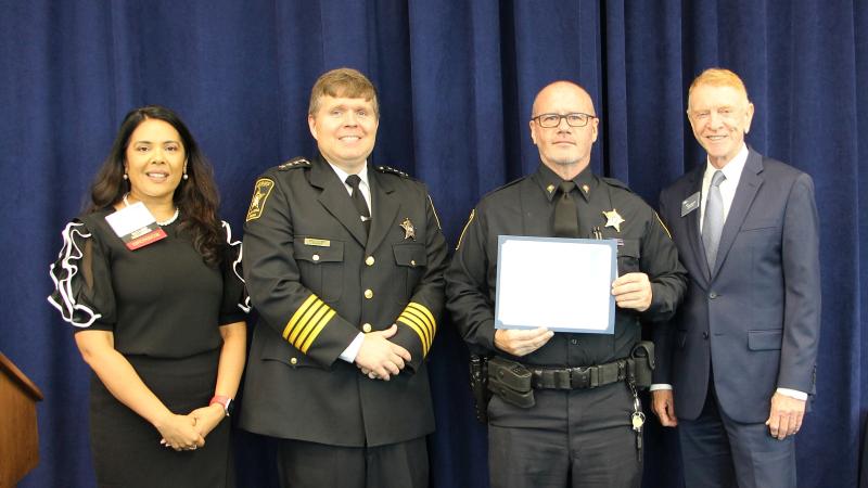 Hospital president, Sheriff, deputy and business association leader standing together with deputy holding a certificate.