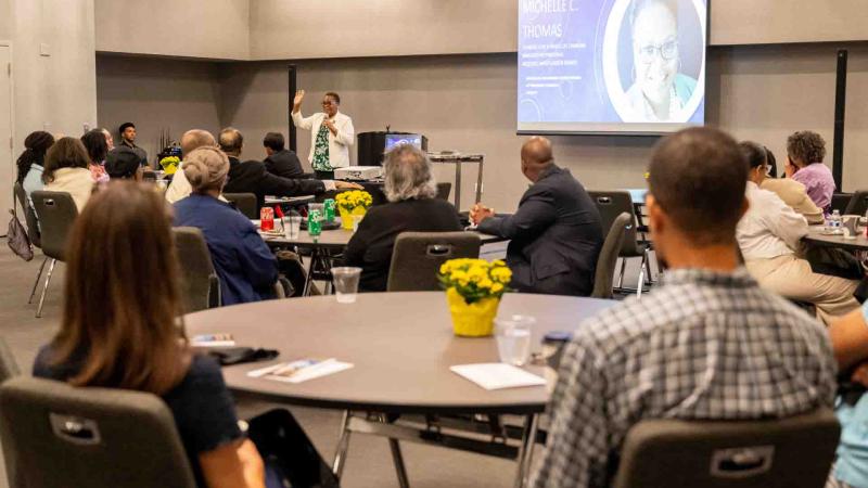 people seated at round table listening to speaker with slides