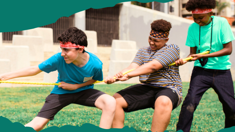 Image of three teen boys outside pulling a rope in a game of tug-o-war