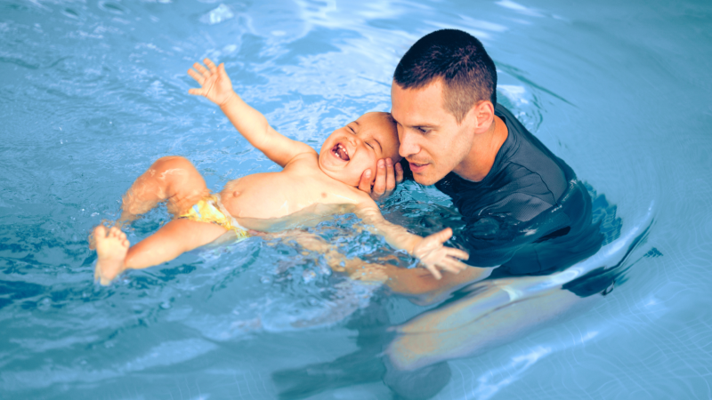 Adult male holding a baby floating in a pool