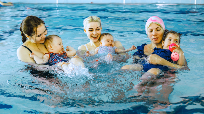 Three female adults holding babies in the water