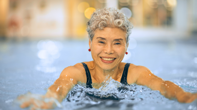 Female senior with red earrings and gray hair smiling at the camera while in an indoor pool