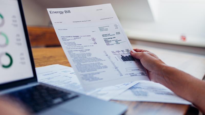 a person holds a paper copy of an invoice next to the computer they are working on