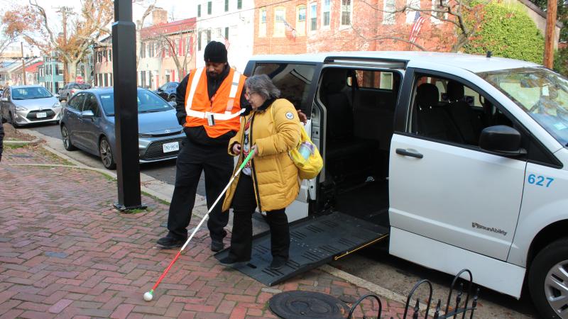 DOT Paratransit operator assisting rider from vehicle to sidewalk.