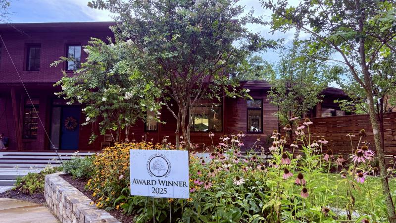 A yard sign that says Award Winner 2025 in front of native plants and trees