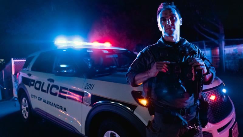 Officer in front of vehicle at night with lights flashing.