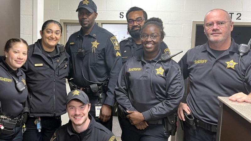 Seven deputies wearing blue uniforms, standing close together and smiling