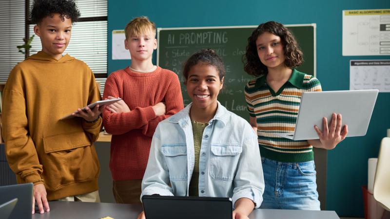 group of teens smiling at the camera while holding electronics