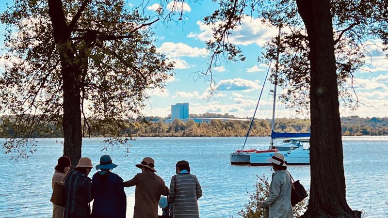 Image of the Potomac river with a group of women standing facing it and boat int he background.