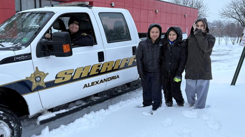 Sheriff in plow truck with three community members nearby in a snowy parking lot