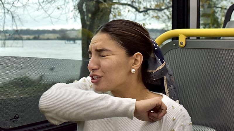 A woman sneezing into her elbow on the bus. 