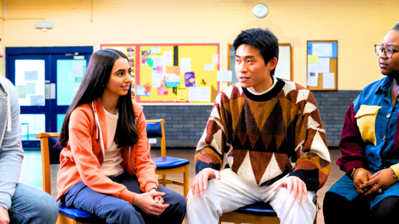 Diverse group of adults sitting in a half circle indoors engaged in conversation