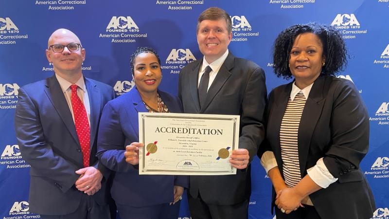 Four corrections executives in business attire standing next to each other with two in the center holding a certificate
